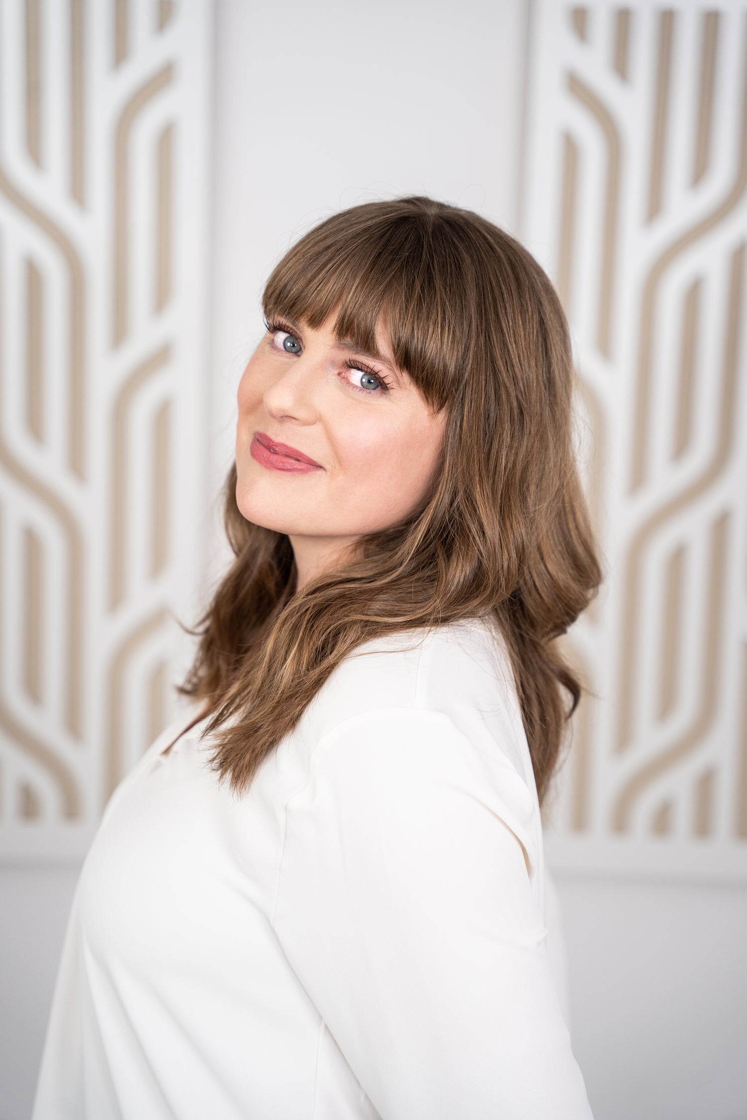 Photo of Founder Michal Morrison showing woman with long brown hair standing in front of a light brown patterned background smiling at camera.