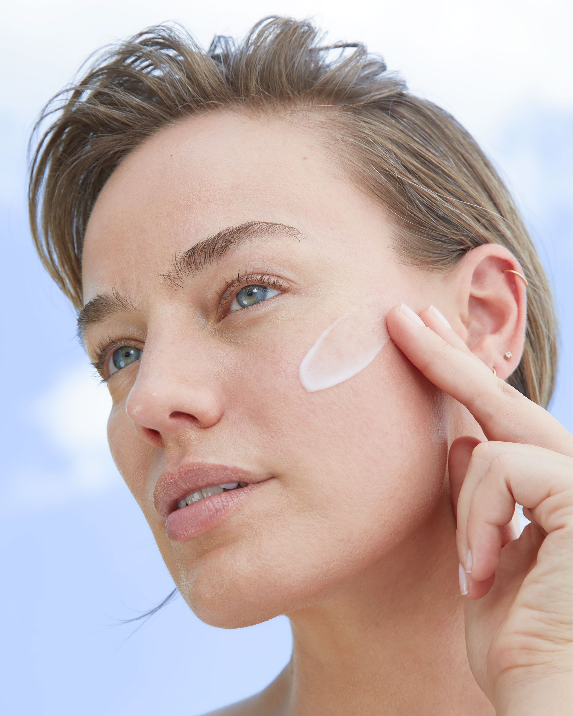 Photo of a woman model applying a smear of Michal Morrison Genesis BSTEM6 Molecular Serum to her left cheek as she faces away from camera