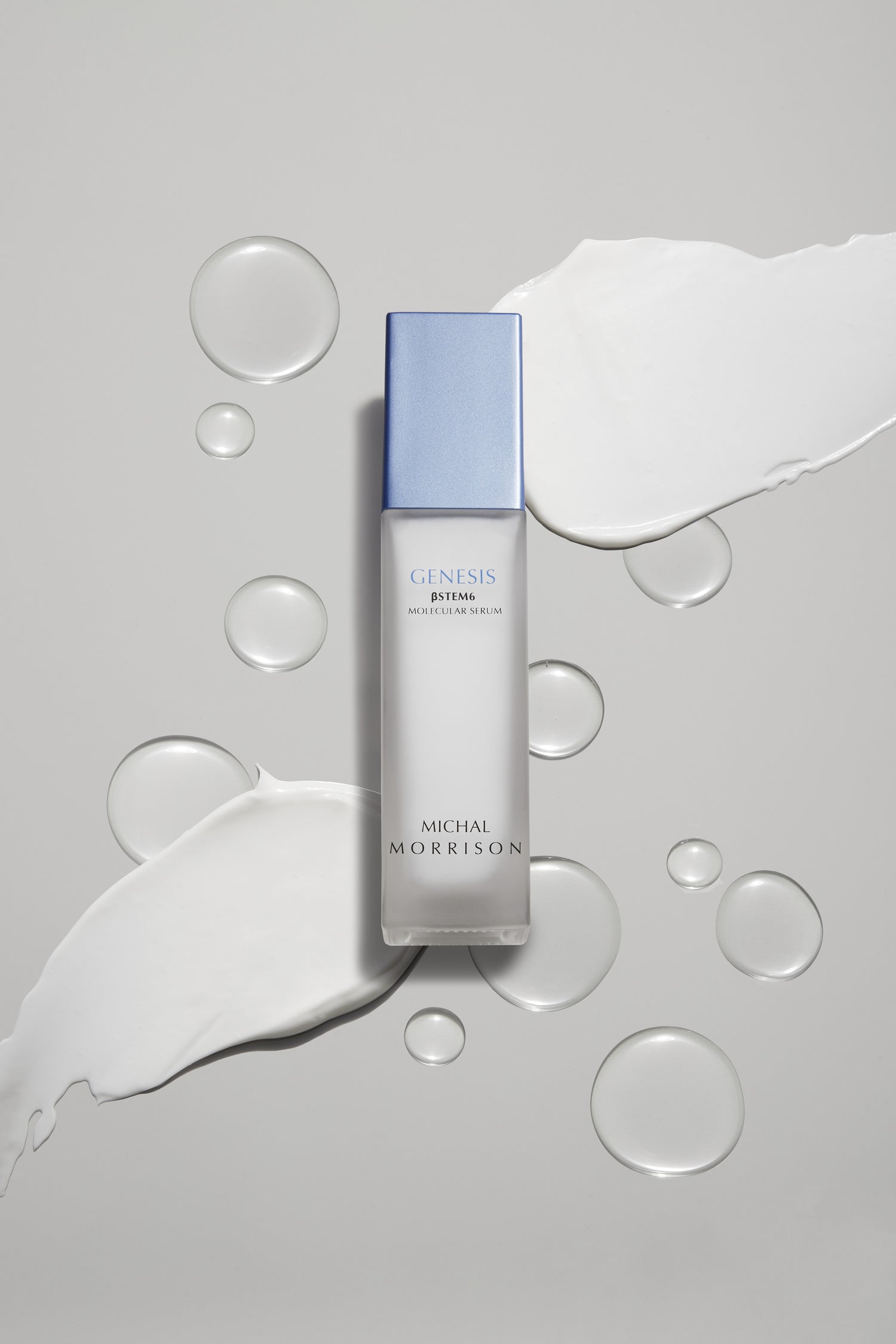 Photo of Genesis BSTEM6 serum in transparent bottle with a periwinkle rectangle cap, sitting on top of a gray background with transparent droplets and white smears of lotion.