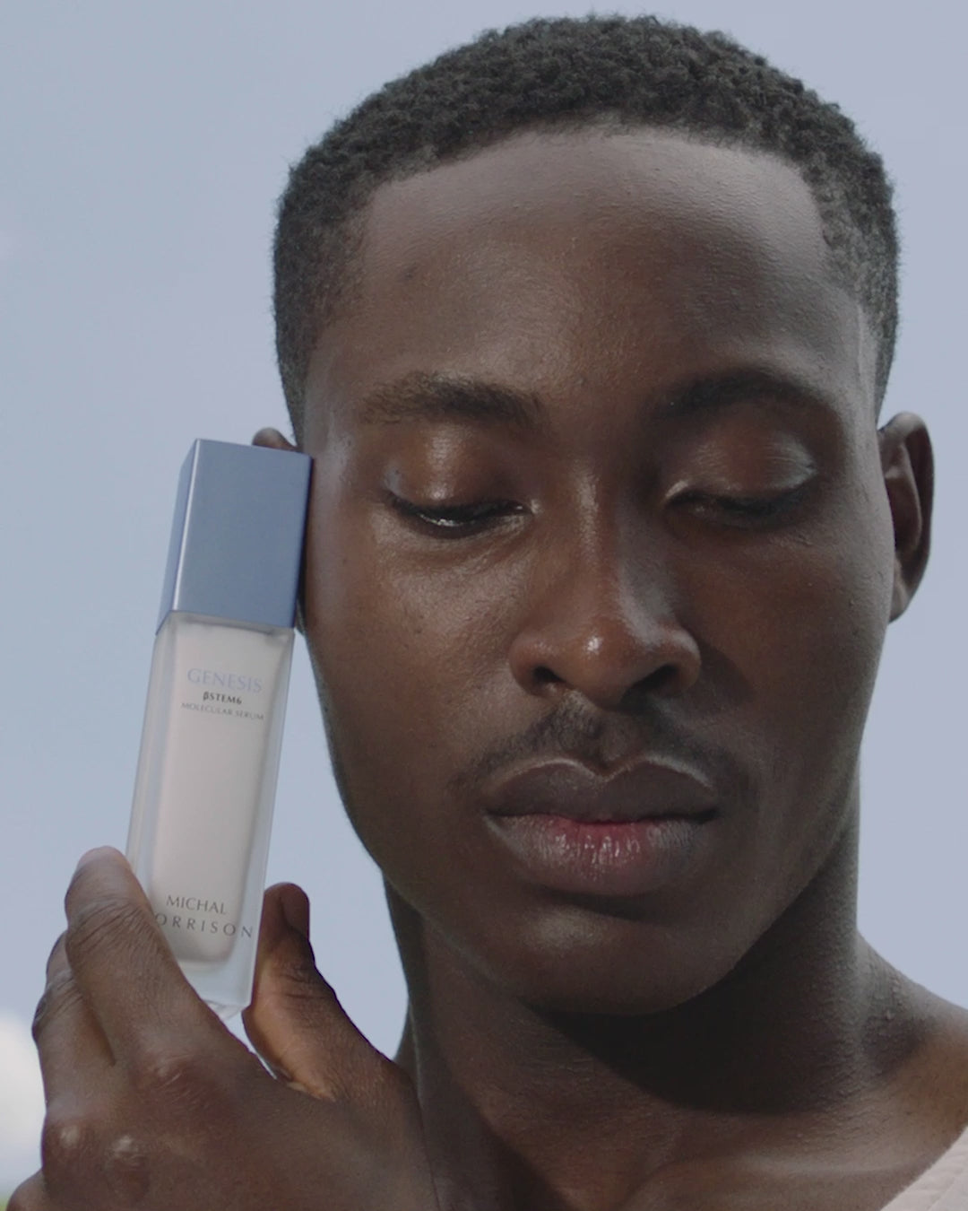 Video showing How-To instructions for using Michal Morrison Genesis BSTEM6 Molecular Serum. Video shows African American male model applying the serum, as well as close up of a set of hands pumping the serum into their palm. Video text reads, "After cleansing, use one pump, Apply to skin on the face and neck, Safe to use in conjunction with any actives such as retinoids and Vitamin C, Radiant. Revitalized. Renewed., Michal Morrison, Where Beauty Begins."